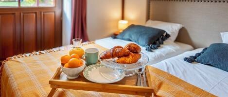 A breakfast tray with croissants, oranges, and a mug on a bed with a plaid blanket.