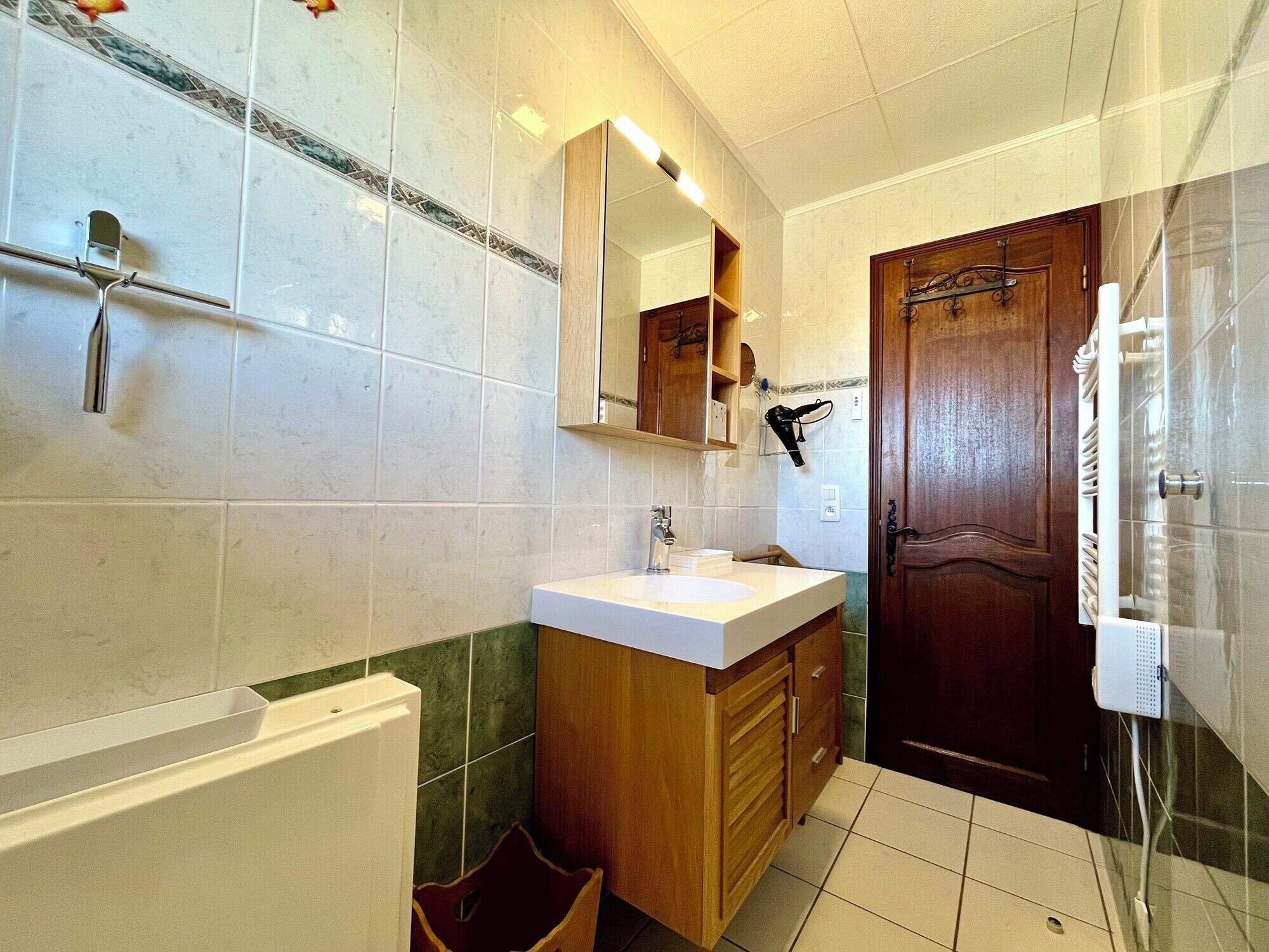 A bathroom with a white sink, wooden vanity, a mirror, a towel rack, and a shower area.