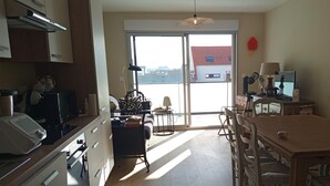 A modern kitchen with a dining area, a large window, and a view of buildings outside. - Nice T3 with balcony - 5 mn from the beach (Merlimont)