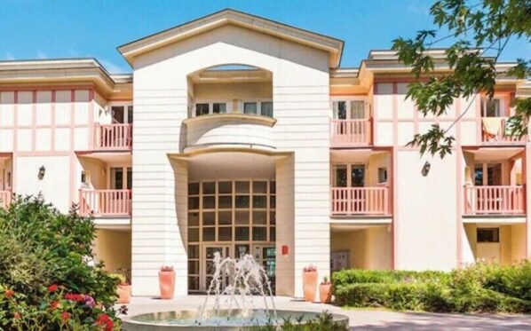 A multi-story hotel with a central entrance, balconies, and a fountain in the courtyard.