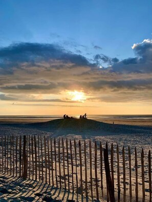 A beach with a wooden fence in the foreground and people sitting on a sand dune in the background during sunset. - T2 apartment in residence with pool (Le Touquet-Paris-Plage)