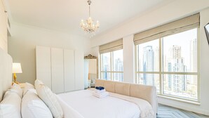 Ein modernes Hotelzimmer mit einem großen Bett, einem Kronleuchter und Blick auf die Stadt durch große Fenster.