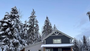 Ein zweistöckiges Haus mit dunkler Fassade und hellem Dach, umgeben von schneebedeckten Bäumen.