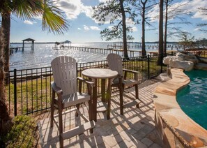 Un espacio de patio con sillas Adirondack y una pequeña mesa redonda, con vista a un cuerpo de agua y un muelle.