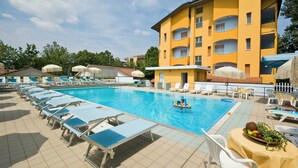 A swimming pool with lounge chairs, a child in a float, and a yellow building with balconies. - Hotel & Residence Parador (Cesenatico)