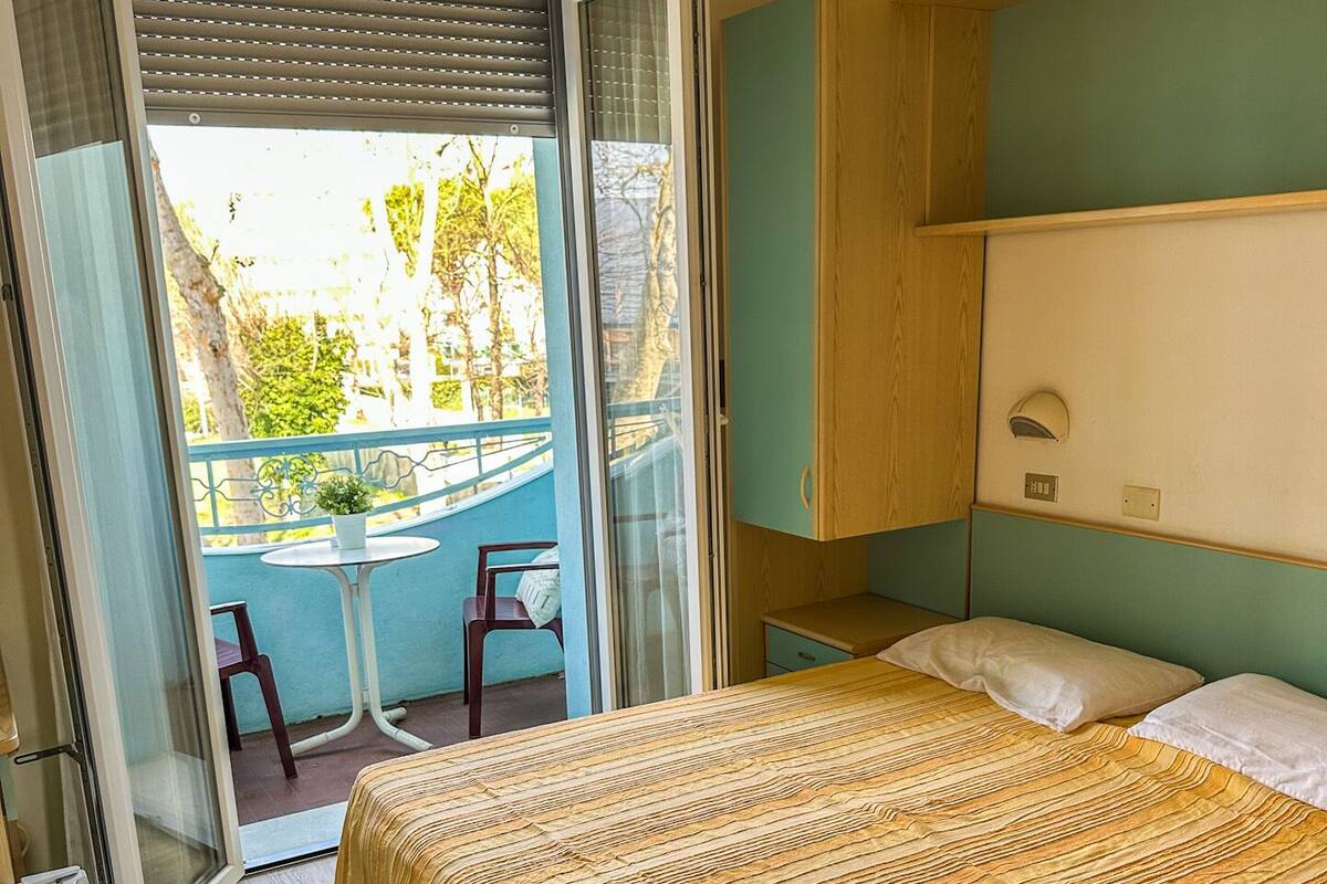 Un dormitorio con cama, una mesita con sillas, una puerta corrediza de vidrio que da a un espacio exterior y un ventilador de techo.