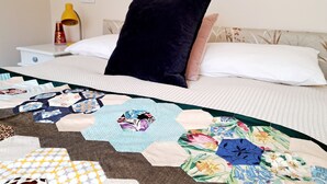 A neatly made bed with a quilt, a bedside table with a lamp, and a wall socket.