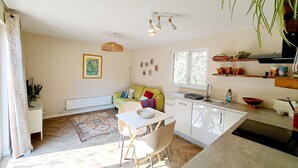 A modern kitchen with white cabinets, a dining area with a table and chairs, a radiator, and a window with a view of greenery.