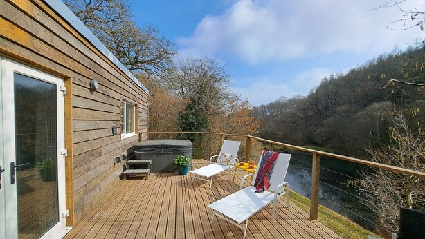 A wooden deck with a hot tub, two white lounge chairs, and a painting on a board.