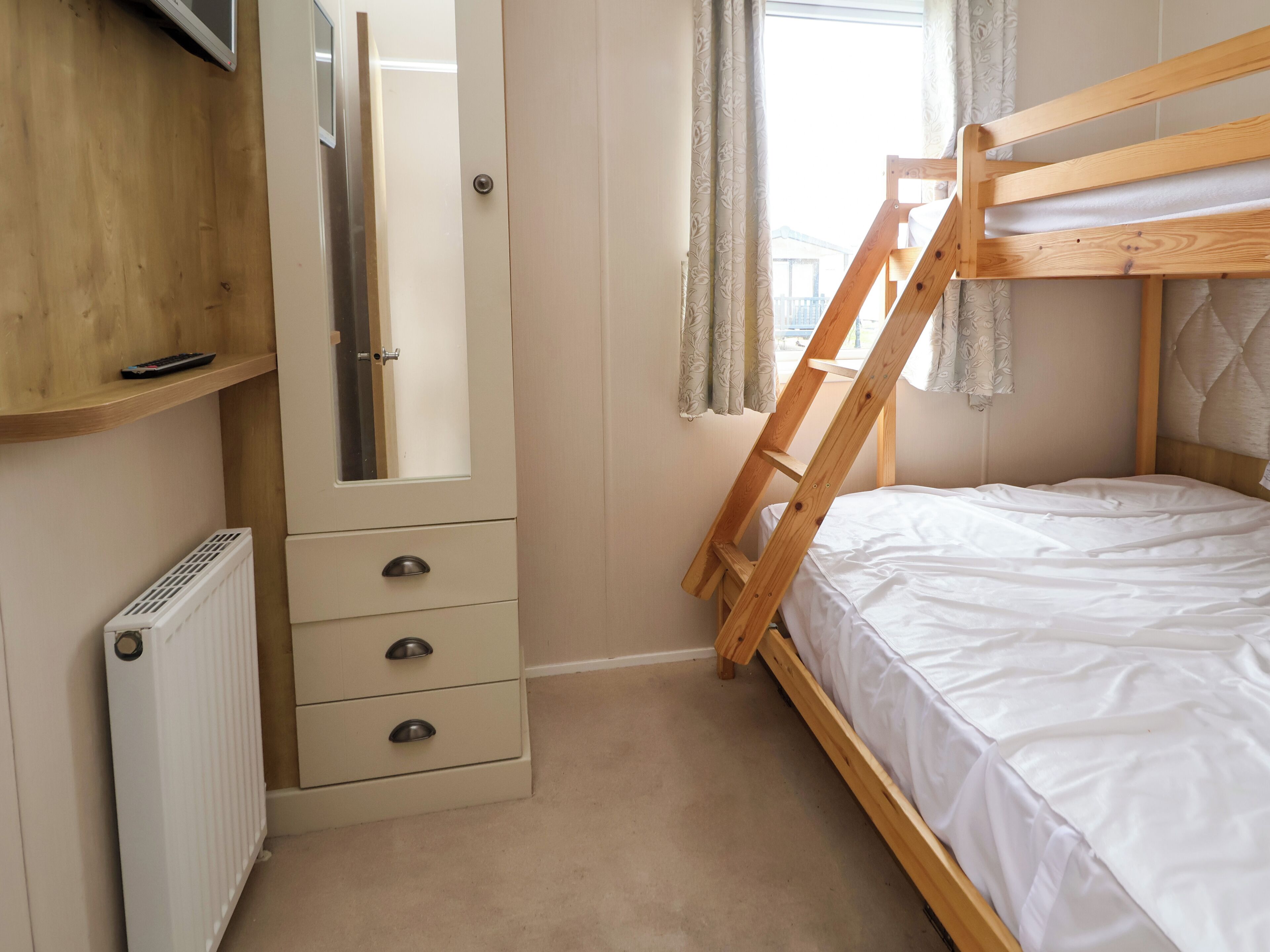 Ein Schlafzimmer mit Etagenbett, Kommode mit Schubladen, Heizkörper und Spiegel.