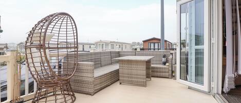 A balcony with wicker furniture, a hanging chair, and a view of neighboring buildings.