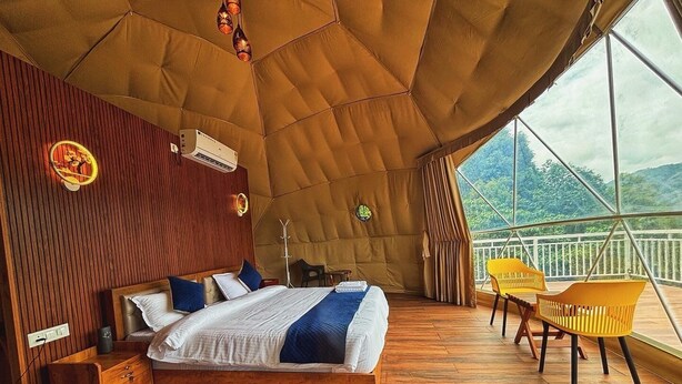 A spacious bedroom with a large bed, wooden floor, and a balcony with yellow chairs.