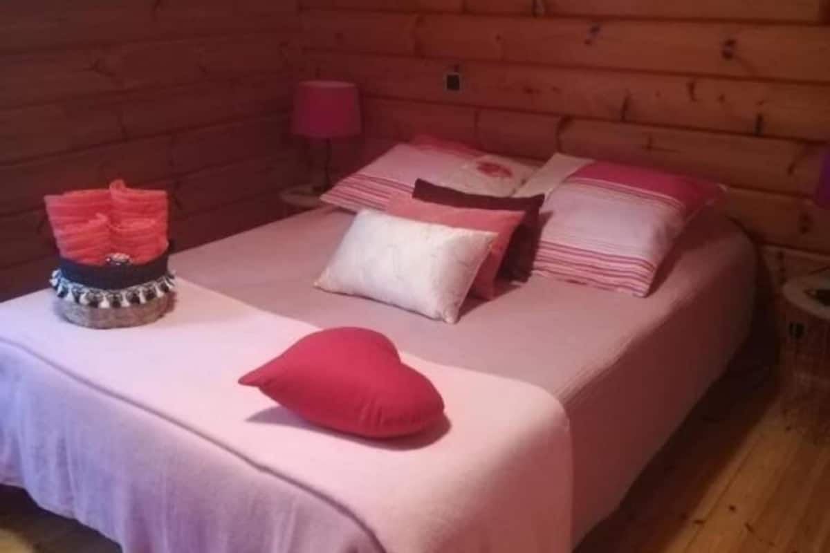 A cozy wooden cabin room with a bed, pillows, a small table with a decorative item, and a wall clock.