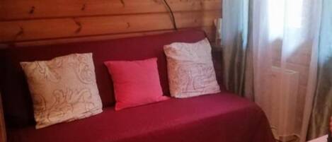 Ein Zimmer mit Holzvertäfelung, einem roten Sofa, einem an der Wand befestigten Fernseher und einem Fenster mit Vorhängen.