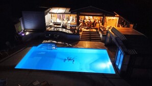 Ein Pool mit Glasboden, umgeben von einer überdachten Terrasse mit Sitzgelegenheiten und einer Bar.