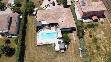 Vista aérea de una zona residencial con piscina rodeada por una terraza, un porche cubierto y un pequeño jardín.