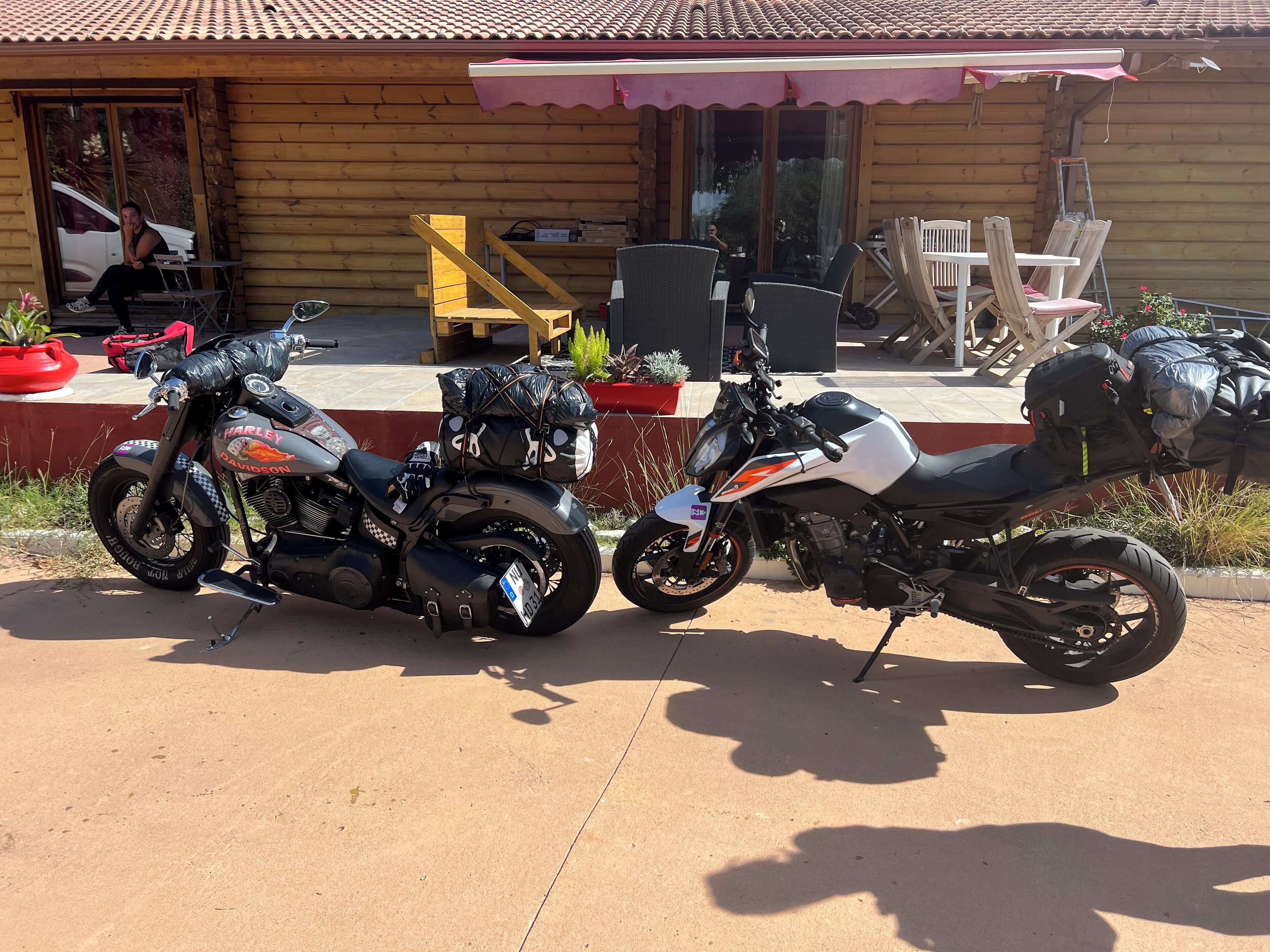 Deux motos sont garées devant un bâtiment en bois dont le toit est recouvert de tuiles.