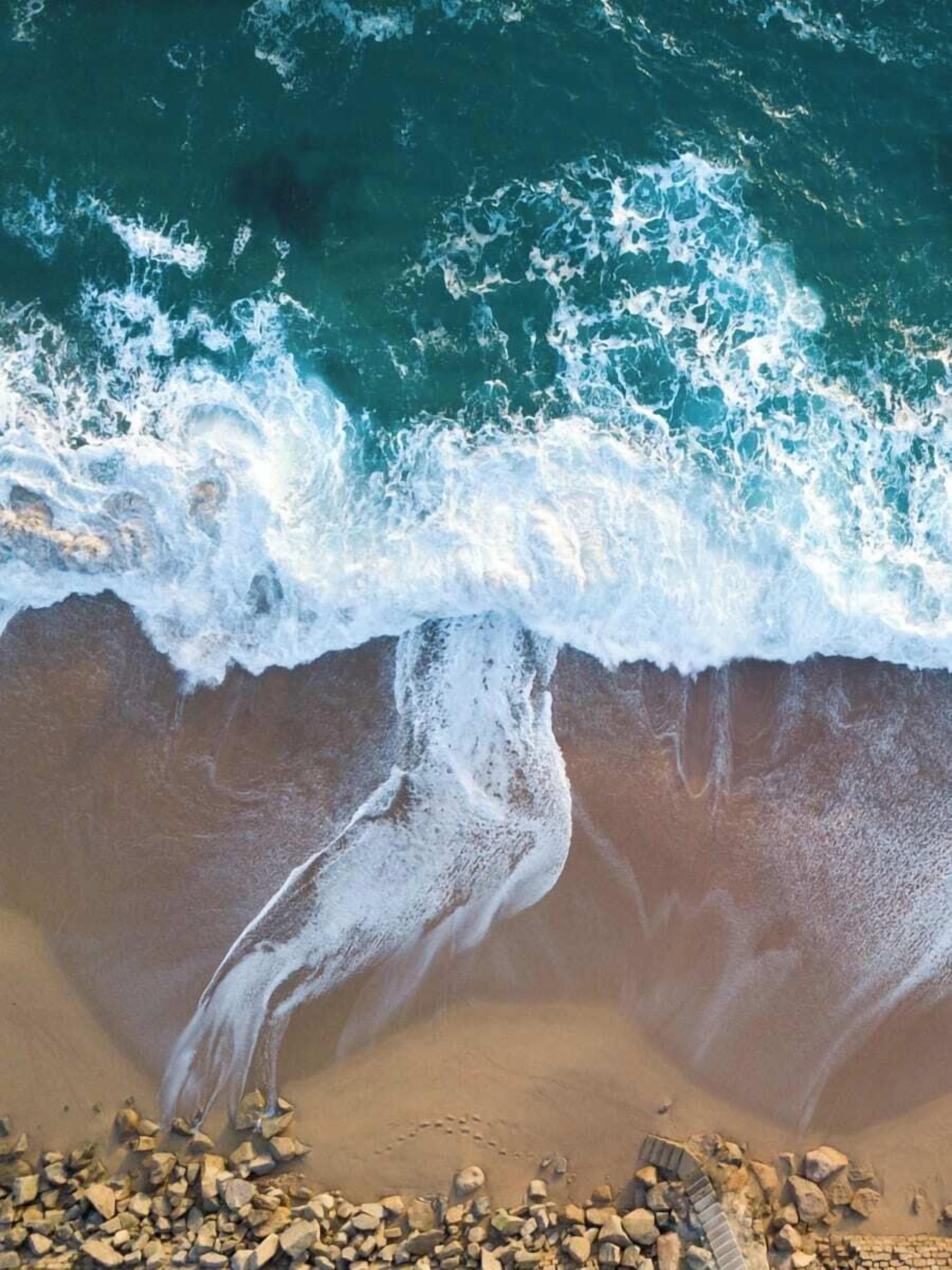 Een strand met golven die op de kust breken, een heldere lucht en verspreide rotsen.
