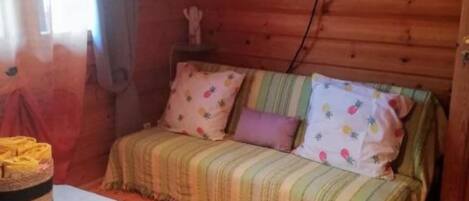 Une chambre confortable de style cabane, avec un intérieur en bois, un lit recouvert d’une couverture à rayures, un téléviseur fixé au mur et une fenêtre avec des rideaux.