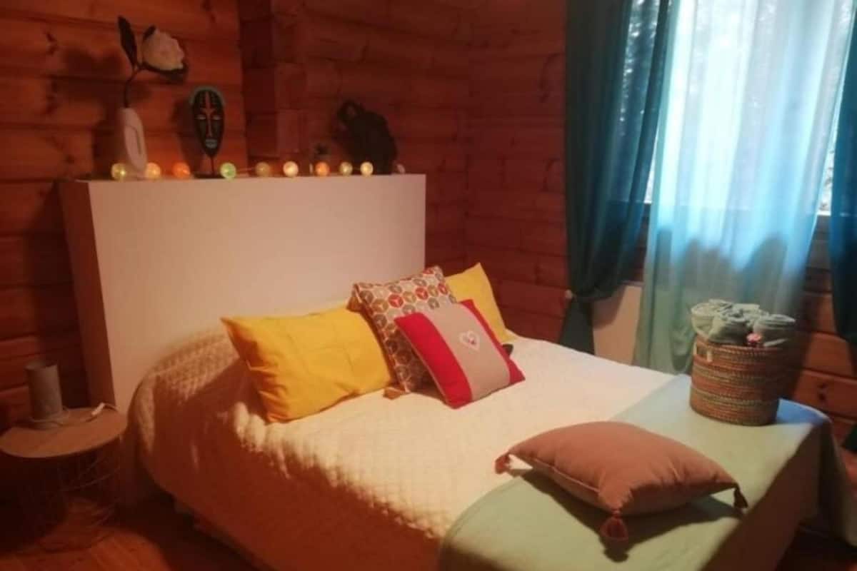 A cozy bedroom with a wooden headboard, a bed with multiple pillows, a bedside table, and a basket on the nightstand.