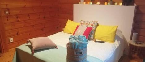 Un dormitorio acogedor de cabaña de madera con una cama, almohadas y una cesta de objetos sobre la cama.