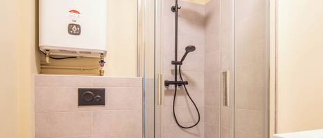 A modern bathroom with a glass-enclosed shower, a toilet, and a built-in heater.