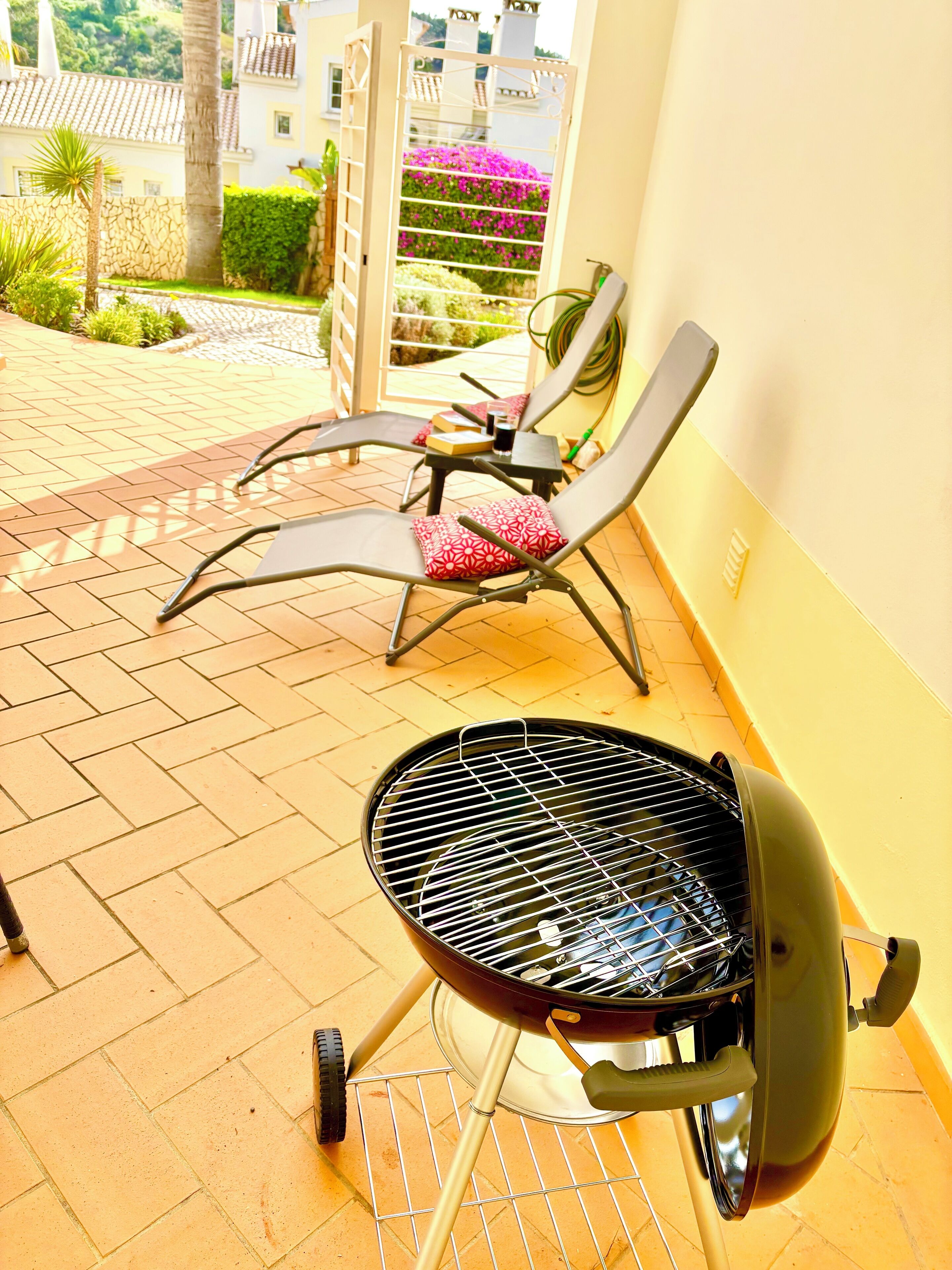 Un patio con una parrilla, dos sillones de descanso y vistas a un jardín y edificios.