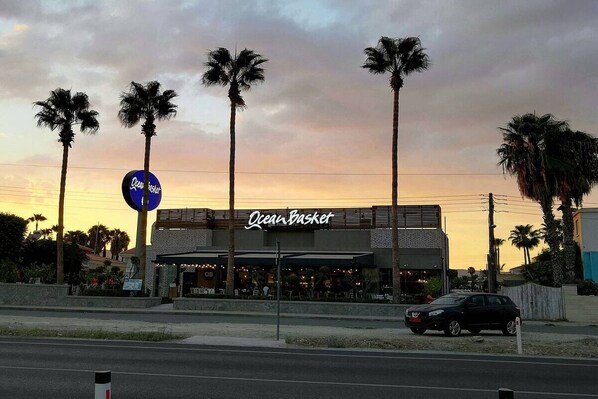 A building with a sign that reads "Ocean Basket" and palm trees in front.