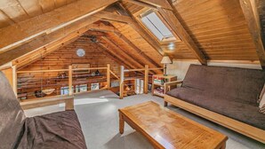 An attic room with wooden beams, a sloped ceiling, a skylight, a sofa, a coffee table, and a bookshelf. - Make Good Choices! LAKE FRONT- 2 King beds and 2 baths (waupaca)