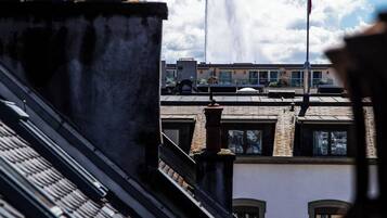 Un edificio con una fuente de agua al fondo, un asta de bandera y un cielo azul despejado con nubes.