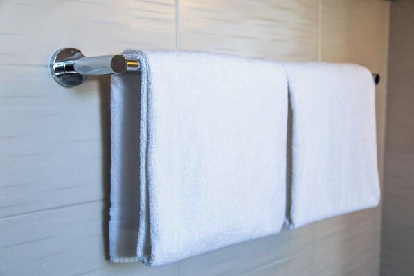 A white towel hanging on a metal towel rack in a bathroom with white tiled walls. - Modern Apartment - AC- 1br-2p- Geneva (Geneva)