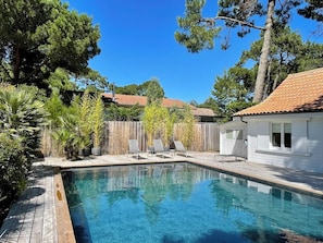 A swimming pool with a wooden deck, surrounded by potted plants and a white building with a tiled roof. - Villa with pool + fantastic terraces A3699 (Lège-Cap-Ferret)
