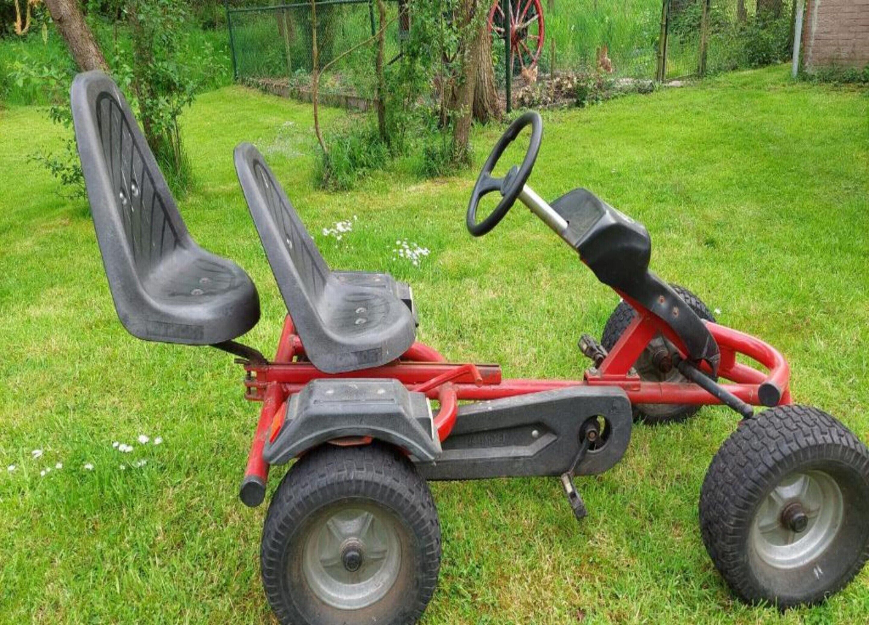 Een rode grasmaaier met twee zitplaatsen en grote achterwielen, geparkeerd op het gras.