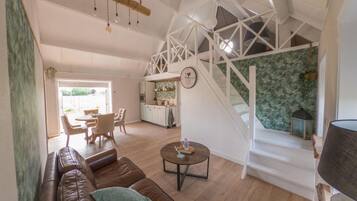 A spacious living area with a brown leather sofa, a round coffee table, and a staircase with white railings leading to an upper level.