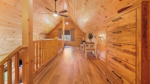 A wooden interior with a sloped ceiling, wooden flooring, a dining table with chairs, and a staircase with a railing. - Seasons on Oak Short walk to best Fly Fishing in Northeast Cozy Cabin Deposit NY (Deposit)