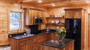 A wooden cabin interior with a kitchen featuring wooden cabinets, a black refrigerator, a microwave, and a sink. - Seasons on Oak Short walk to best Fly Fishing in Northeast Cozy Cabin Deposit NY (Deposit)
