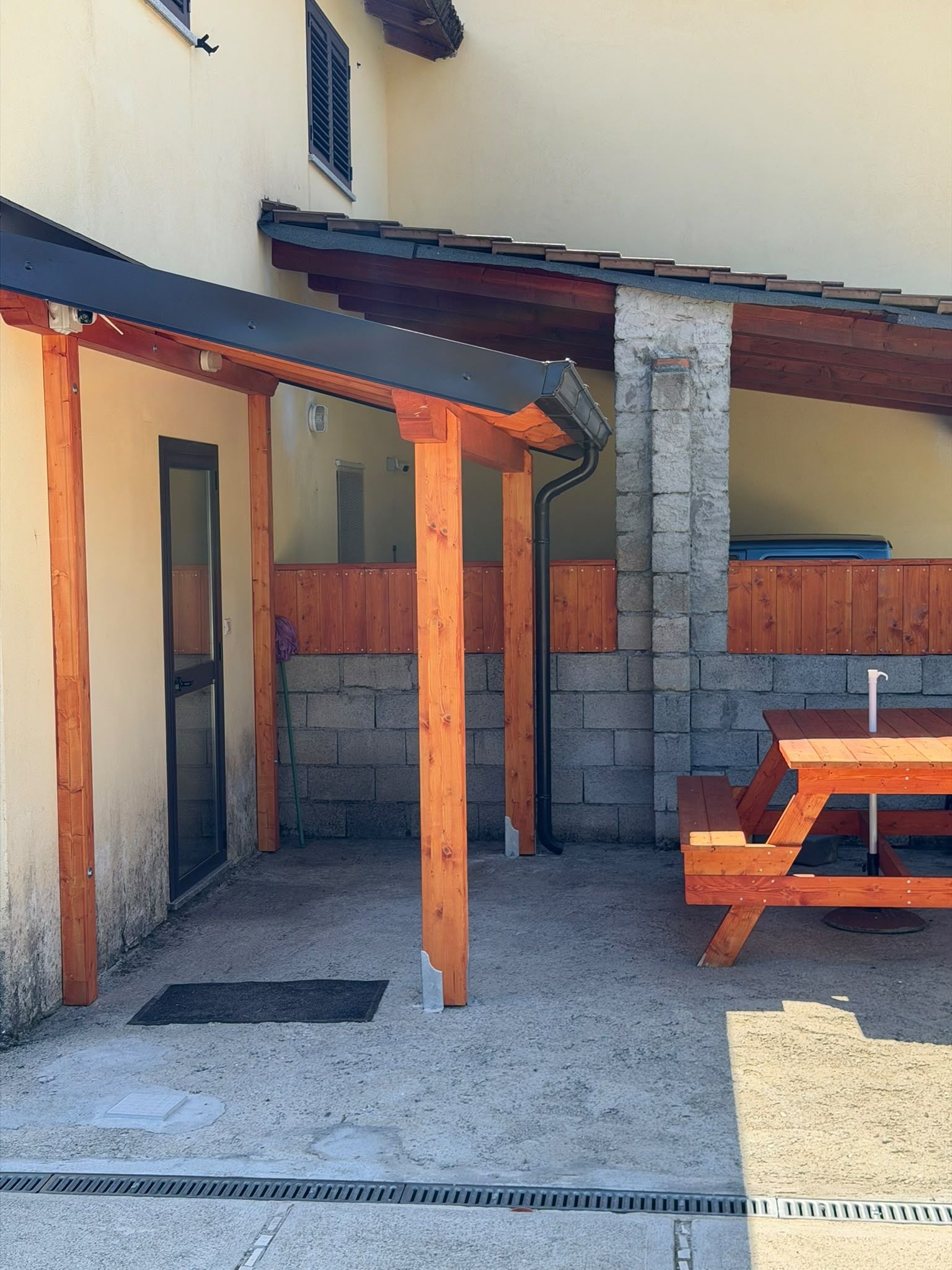A covered outdoor area with a stone wall, wooden pillars, and a picnic table.