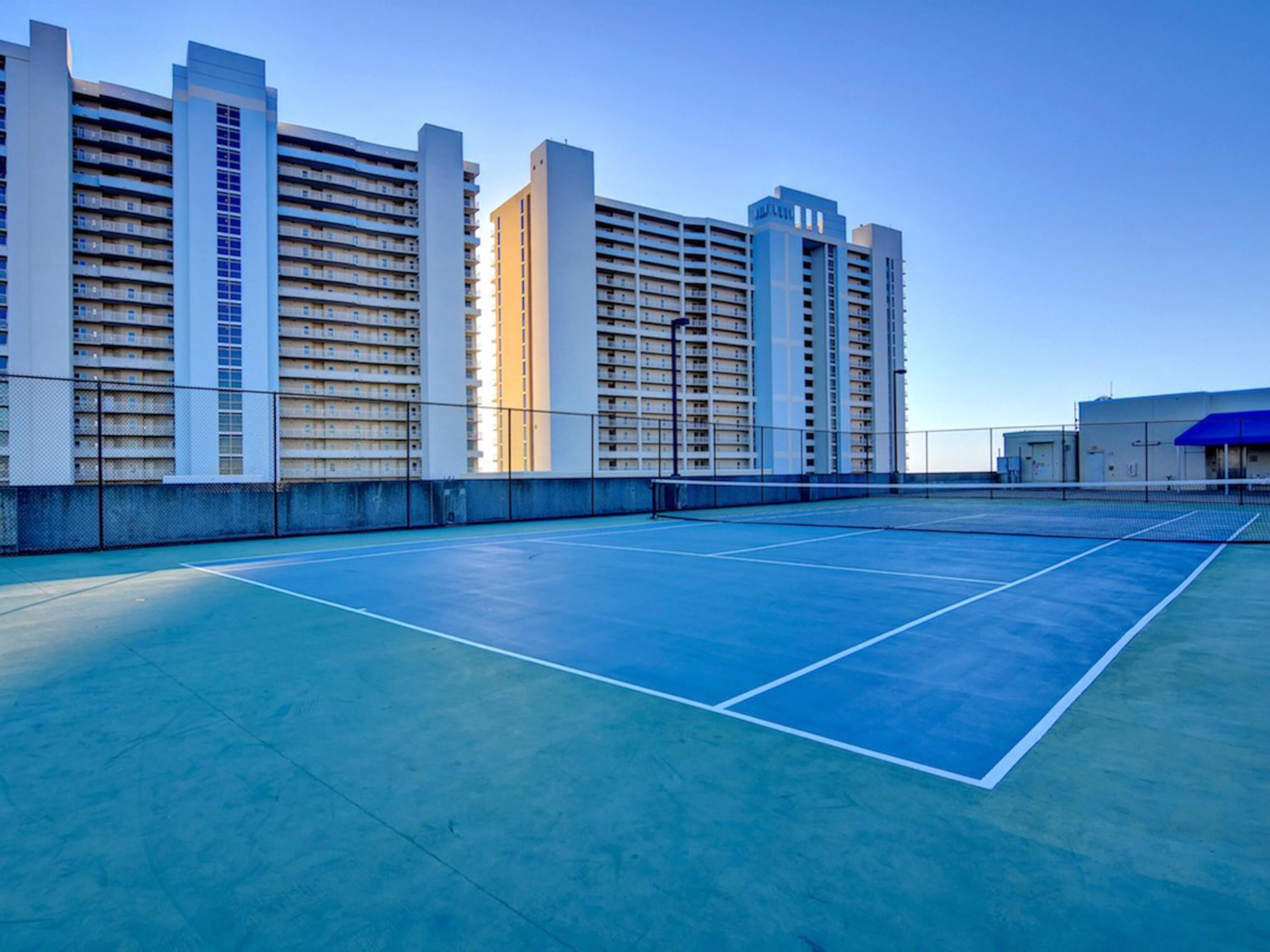 Een tennisbaan met een net, omringd door hoogbouw.