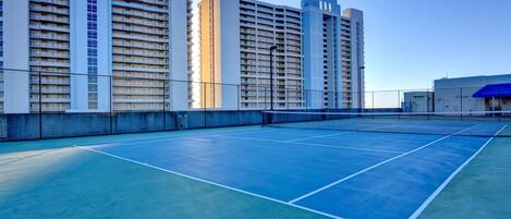 Een tennisbaan met een net, omringd door hoogbouw.