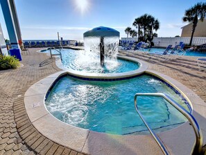 A pool area with a central water feature, lounge chairs, and a view of the ocean. - Majestic Beach Towers I #1505 by Resort Collection (Panama City Beach)