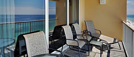 A balcony with a glass table and four chairs, overlooking a beach.