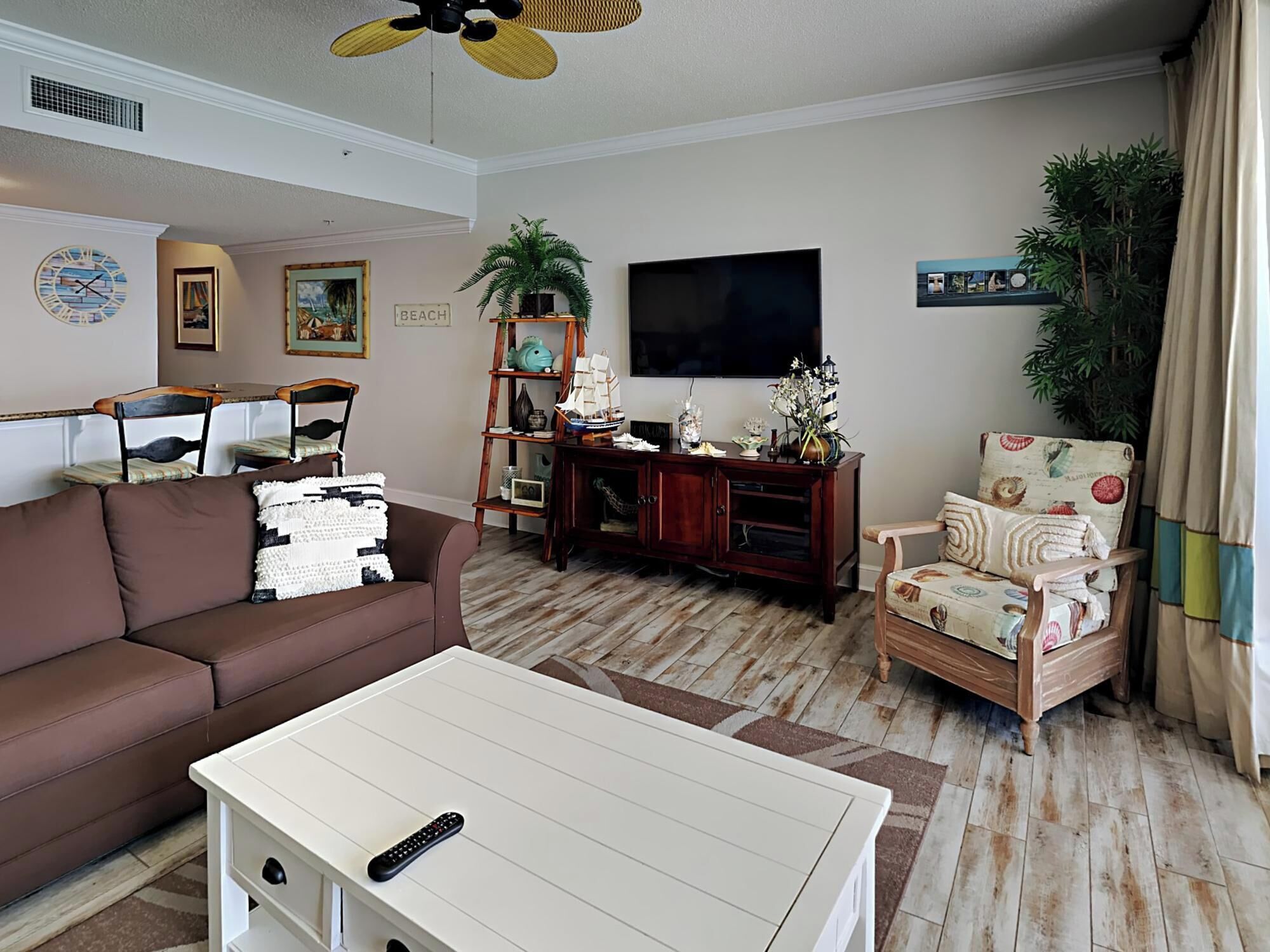 A living room with a brown sofa, a white coffee table, a wooden entertainment center, a television, and a plant.