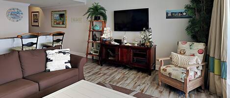 A living room with a brown sofa, a white coffee table, a wooden entertainment center, a television, and a plant.