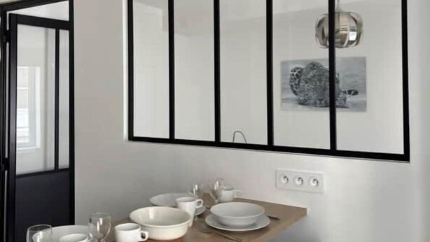A dining area with a wooden table set for four, a black-framed mirror above, and a black chair. - TIGER ROOM - Studio Gailleton Place Bellecour (Lyon)
