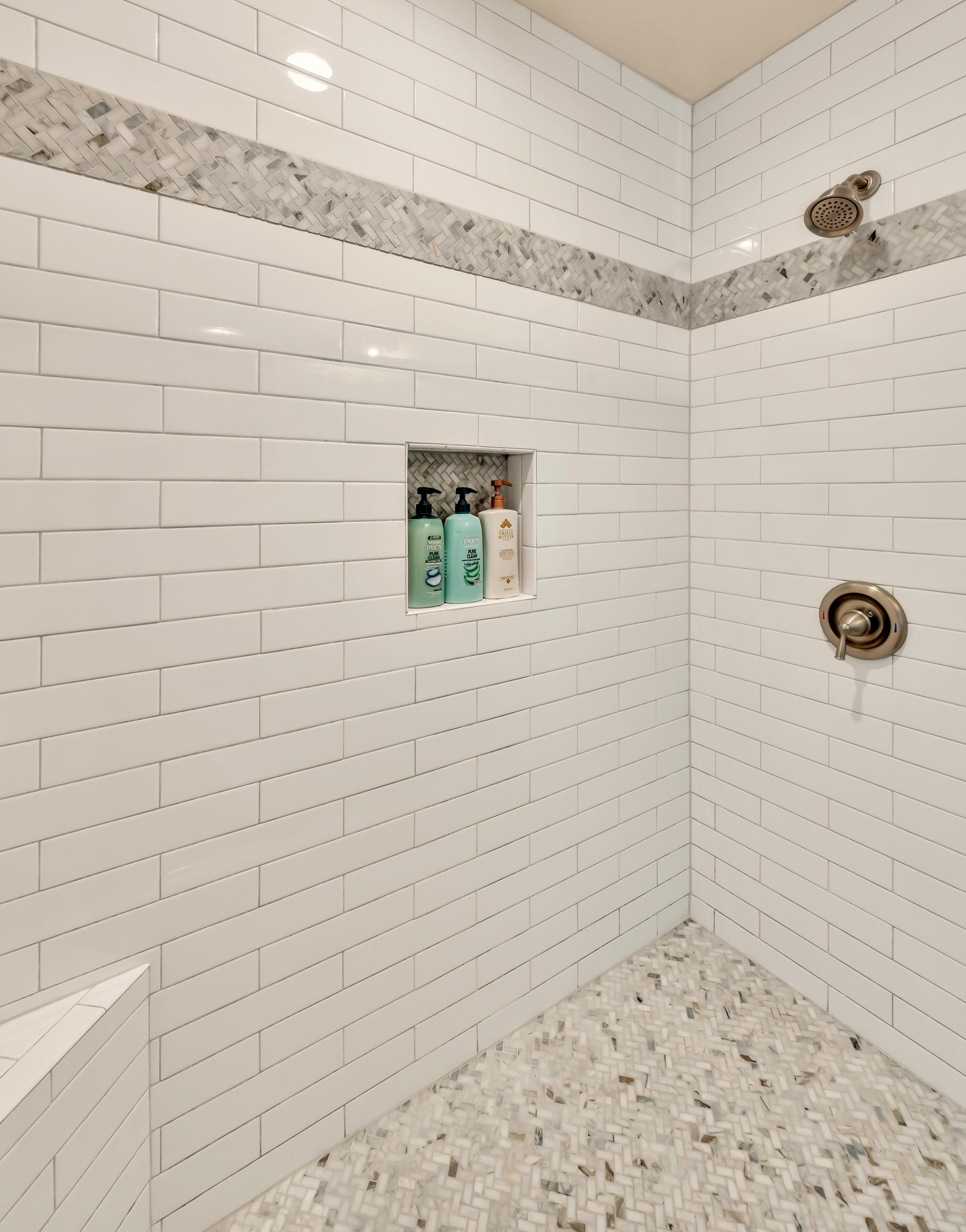 A shower area with white subway tiles, a marble accent wall, and a built-in shelf with toiletries.