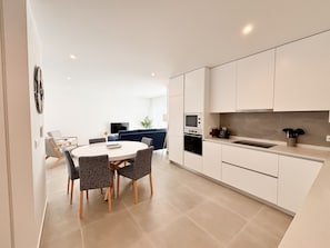 A modern kitchen with white cabinets, a round dining table with chairs, and a built-in oven.