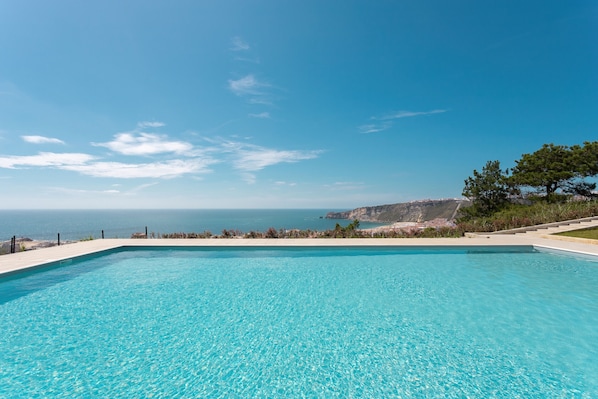 A clear blue swimming pool with a view of the sea and a rocky coastline.