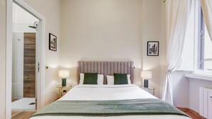 Une chambre d’hôtel bien rangée, avec un lit, deux tables de chevet dotées de lampes, une tête de lit et une fenêtre avec des rideaux.