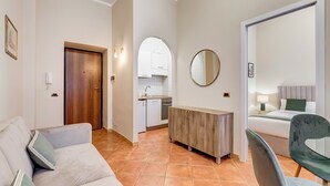 Un salon moderne avec un canapé, une console en bois, un miroir rond et un lit agrémenté d’un coussin vert.