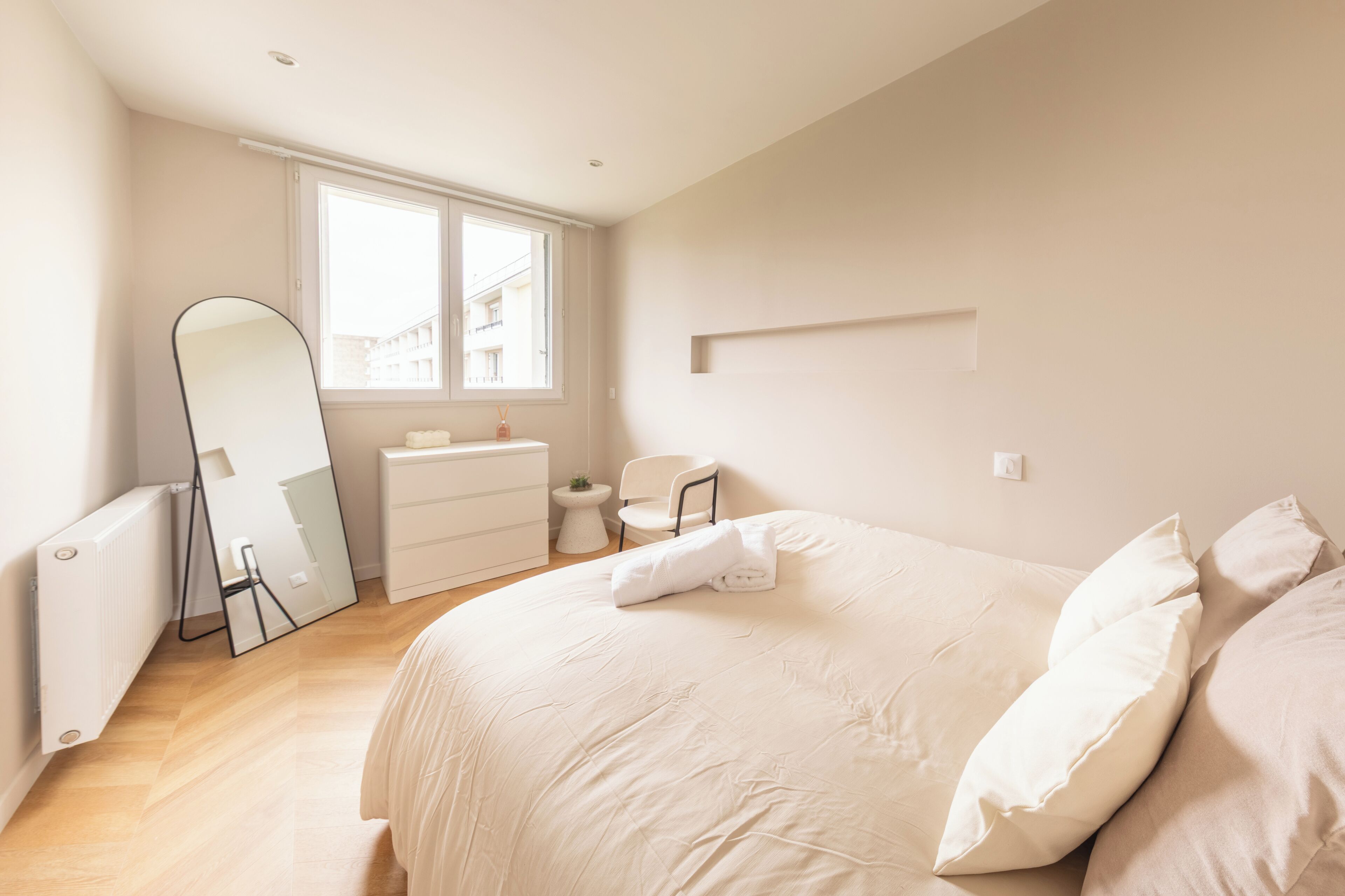 A bedroom with a large bed, a dresser, a chair, a mirror, and a window.